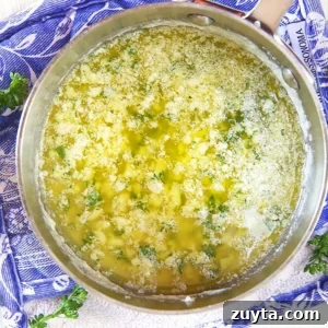 Garlic butter sauce in a saucepan on a blue and white potholder.