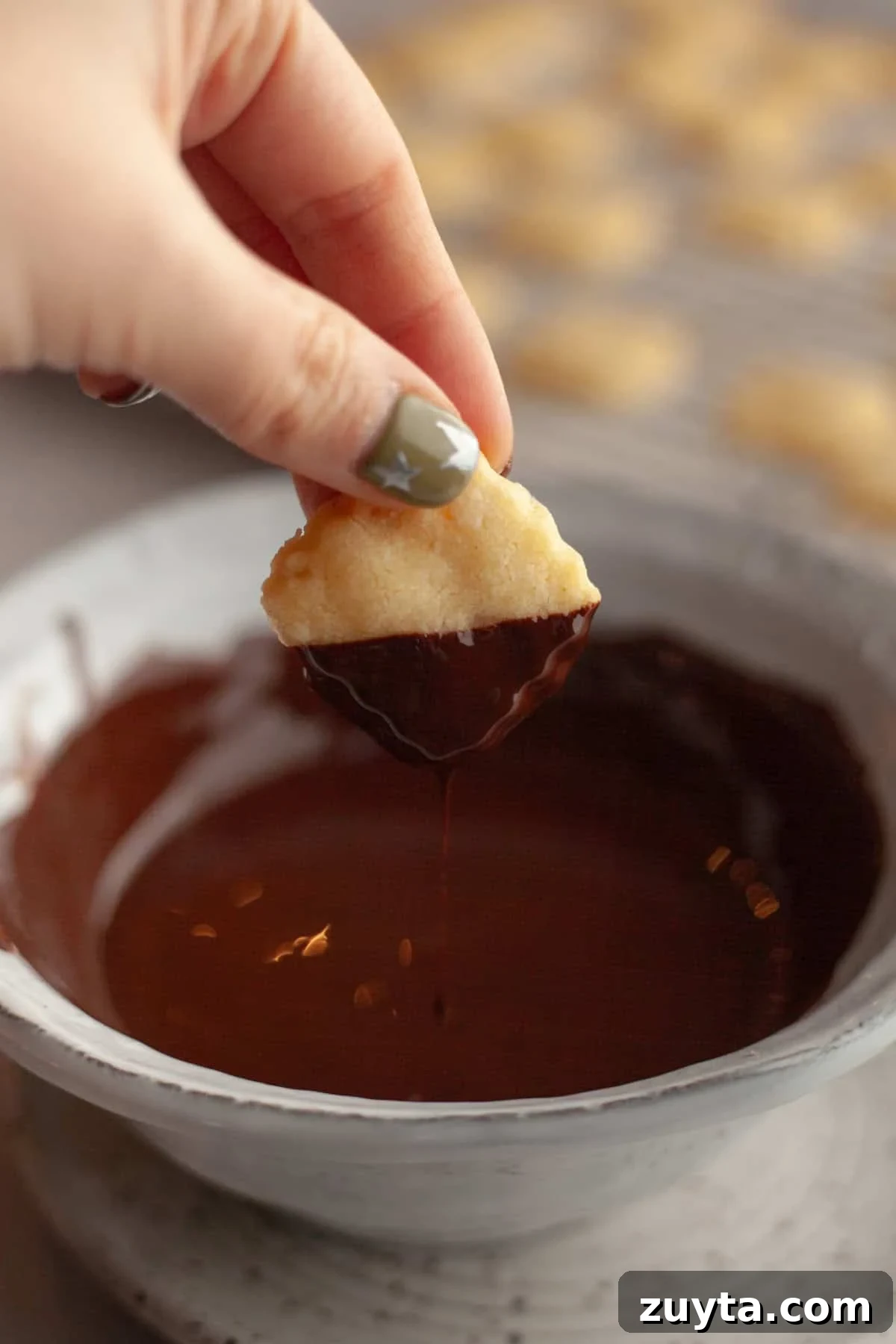 Double-Ginger Shortbread Cookies Recipe 9 A hand dipping a shortbread cookie in melted chocolate.