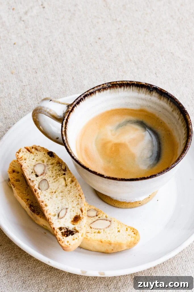 Crisp Fig and Almond Biscotti Recipe 2 Two pieces of almond biscotti on a plate next to a cup of coffee.