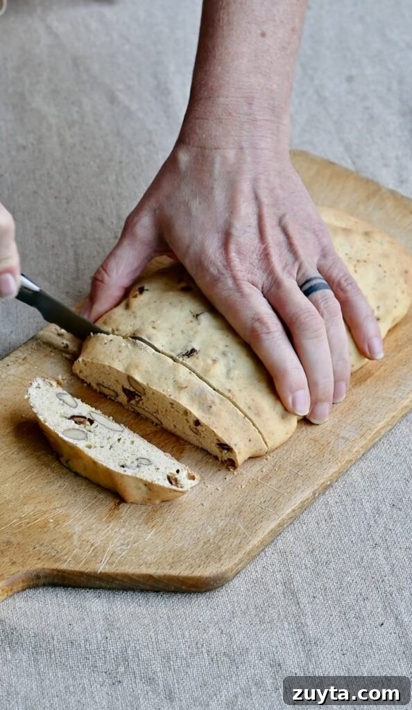 Crisp Fig and Almond Biscotti Recipe 8 A baked biscotti log being cut into slices on a cutting board.