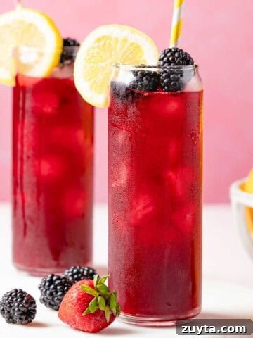 two glasses of berry lemonade garnished with lemon and blackberries.
