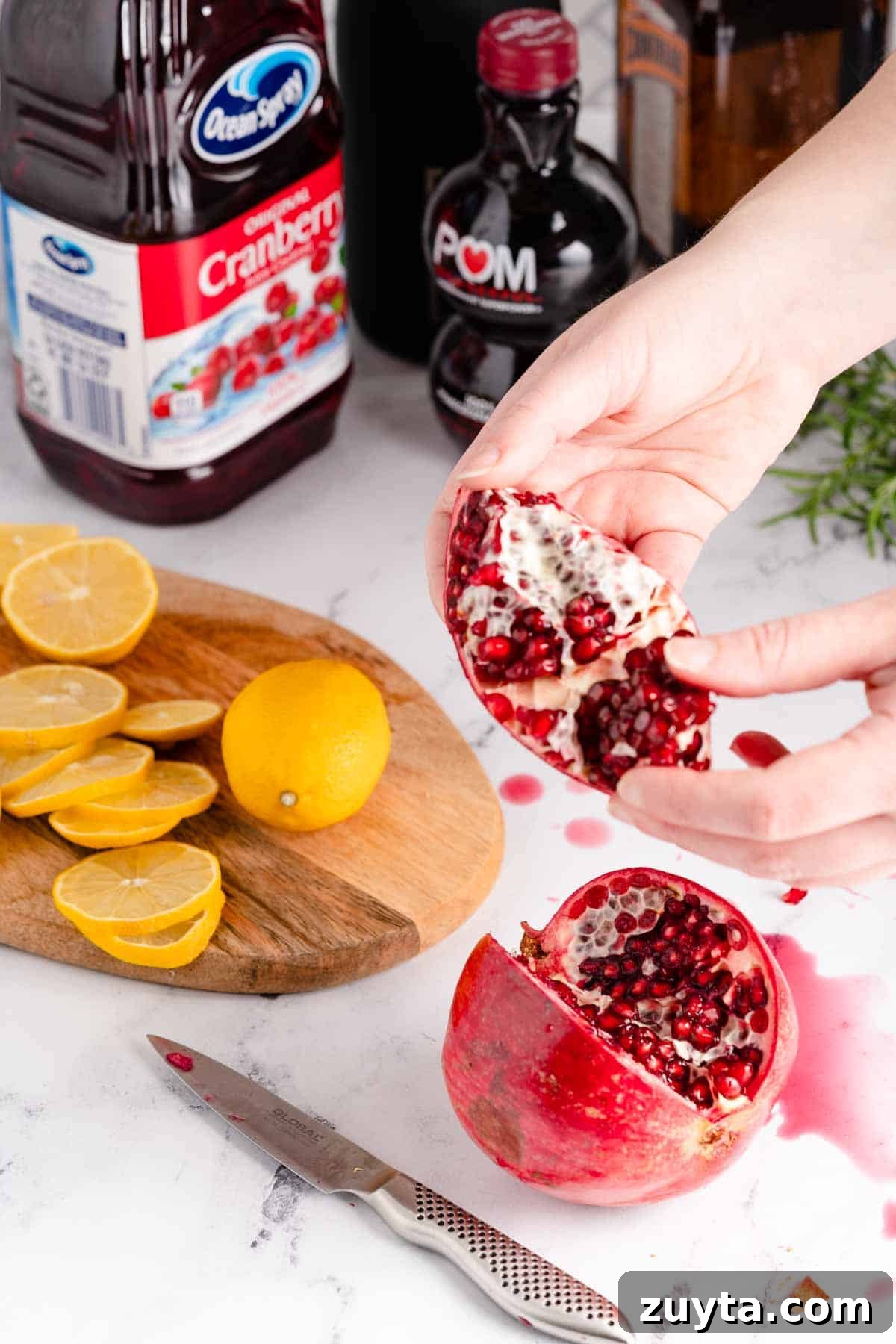 Sparkling Pomegranate Cranberry Punch Recipe 4 hands pulling section of pomegranate apart with sliced lemons and juices in the background