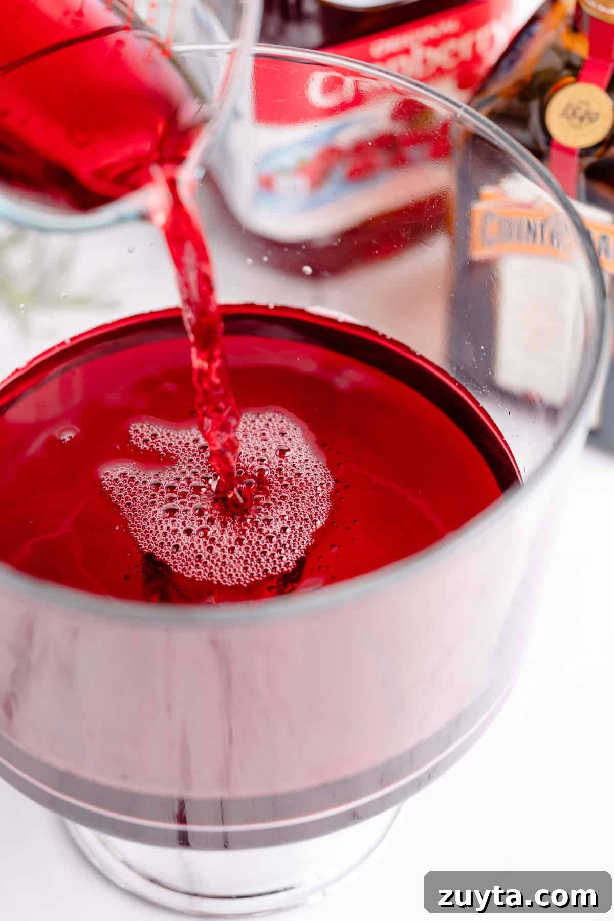 Sparkling Pomegranate Cranberry Punch Recipe 5 cranberry juice pouring into glass bowl with bottle of juice in the background