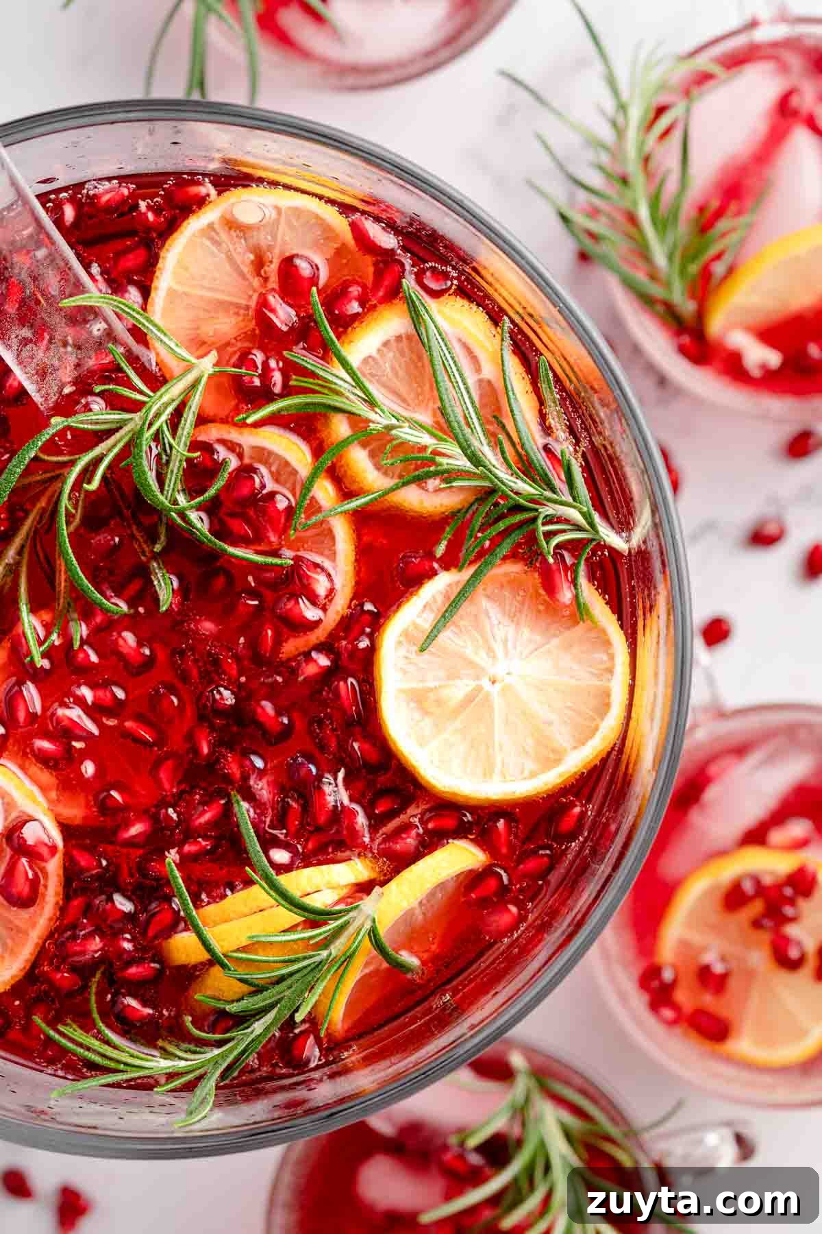 Sparkling Pomegranate Cranberry Punch Recipe 8 punch in bowl garnished with pomegranate seeds lemon slices and rosemary with punch cups on the side
