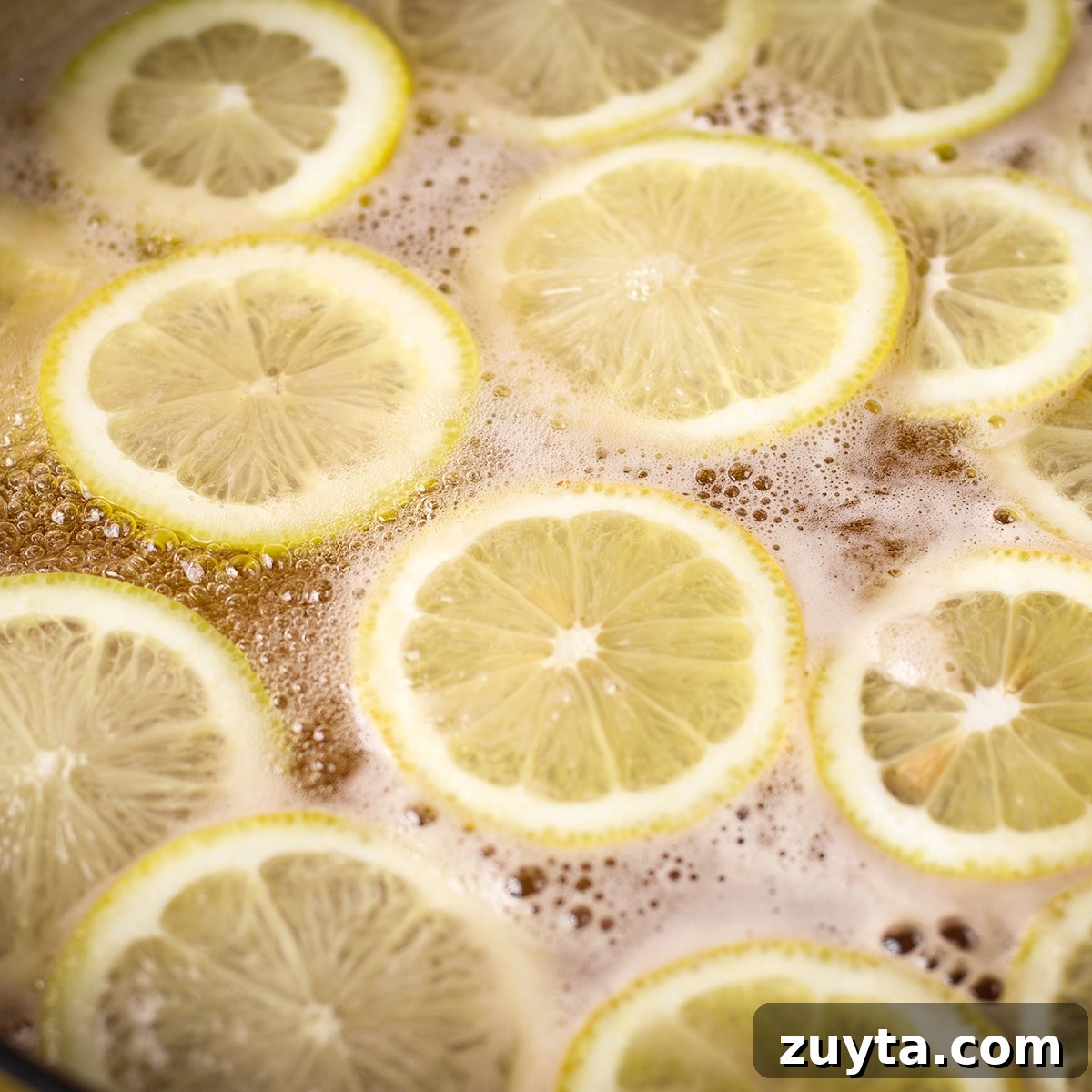 How to Make Candied Lemon Slices for Garnish and Snacks 5 Lemon slices simmering in a pan filled with sugar water.