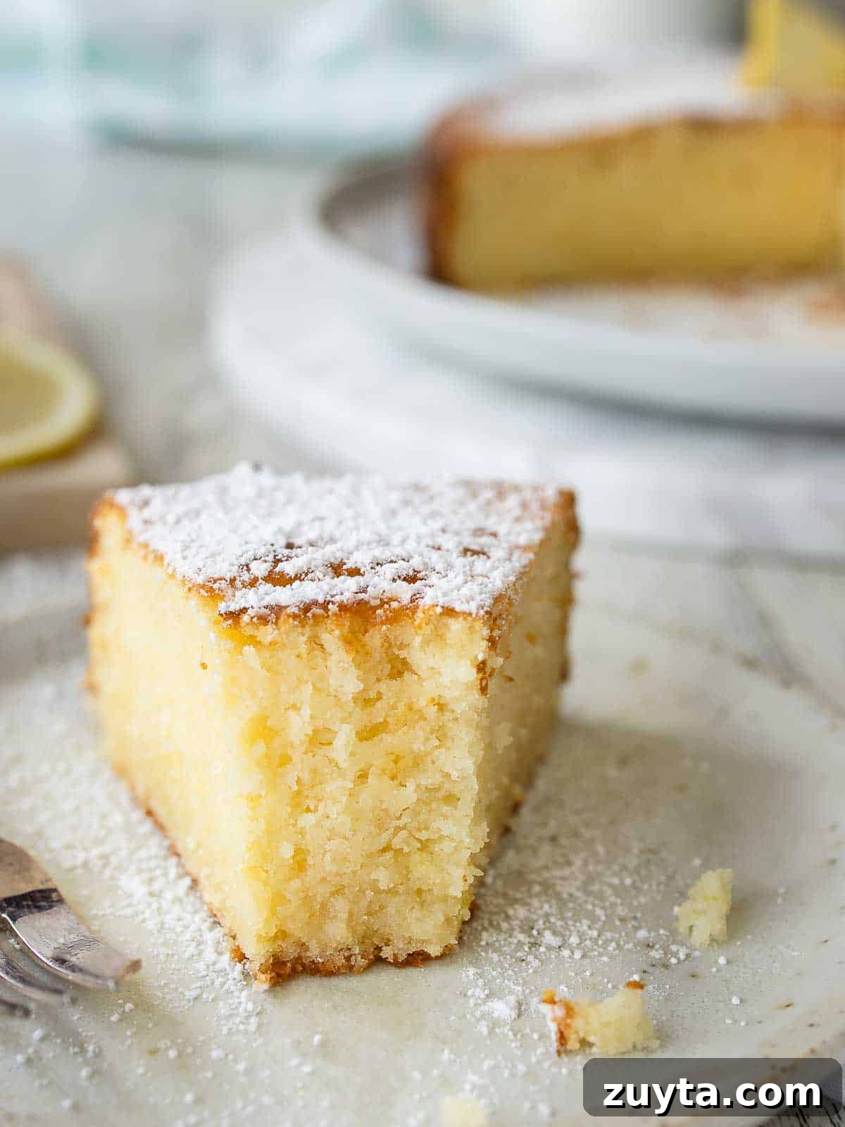 Lemon Ricotta Cake Recipe - Zesty Italian Dessert 2 A half eaten wedge of lemon and ricotta cake on a plate with the whole cake in the background.