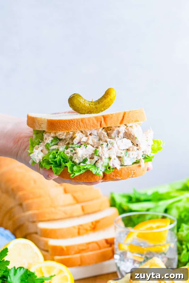 How to Make a Classic Tuna Salad Sandwich 5 A hand holding half of a tuna salad sandwich with creamy tuna salad and lettuce.