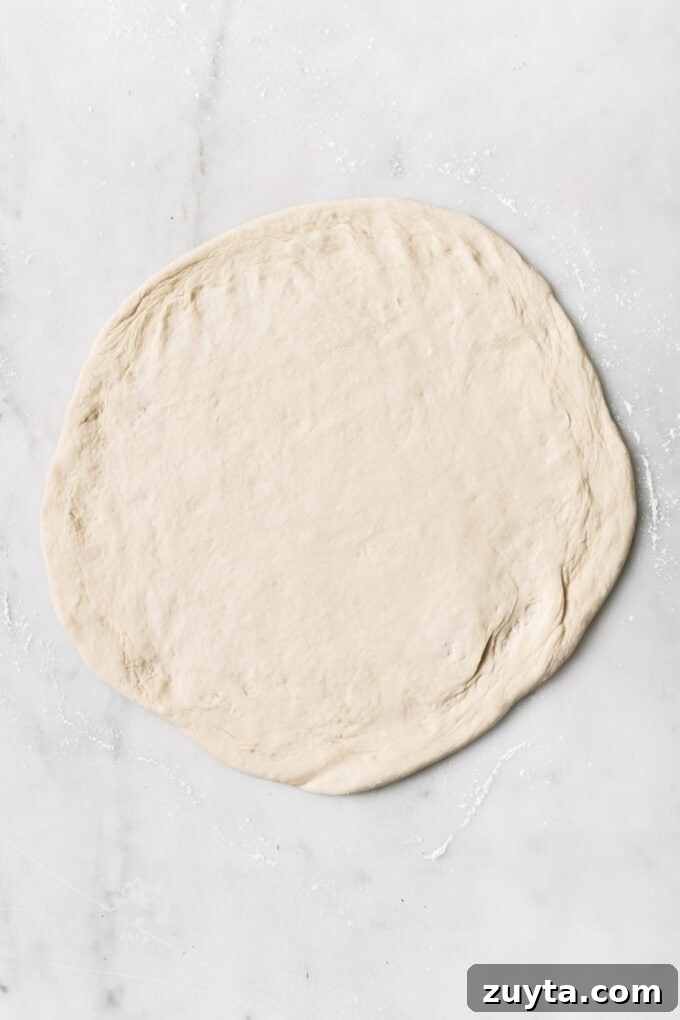 rolled out pizza dough on a marble counter