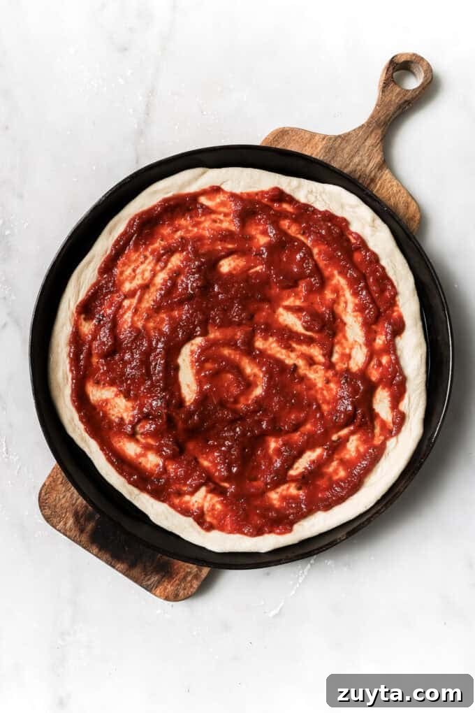 pizza dough topped with pizza sauce on a wood board