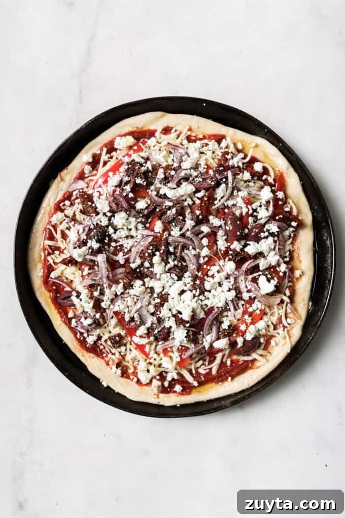 pizza dough with mediterranean toppings in a black pizza dish