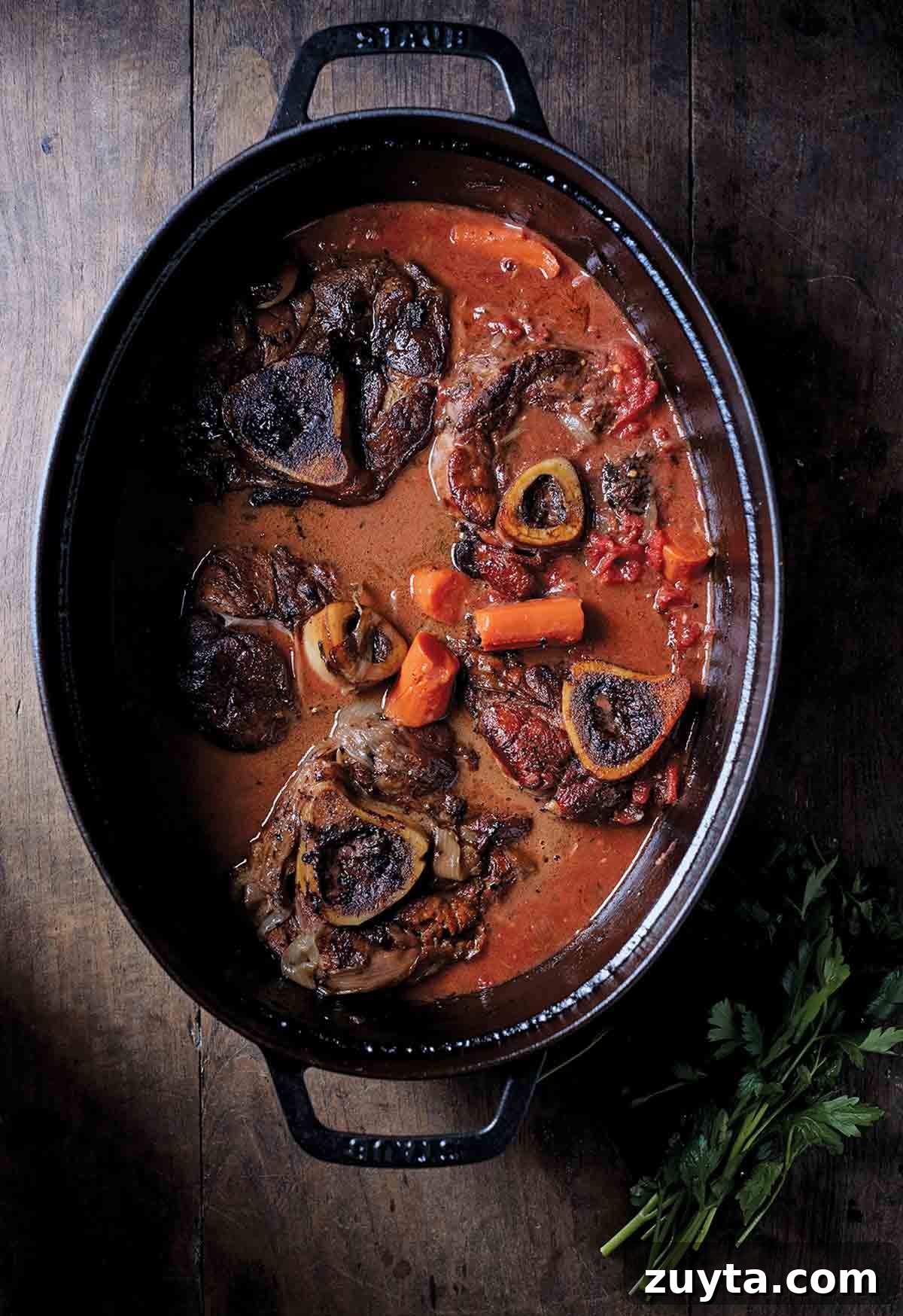 Braising Explained: What It Is and How to Braise 2 A black oval pot with five veal Rosso buck, carrots, and tomato sauce
