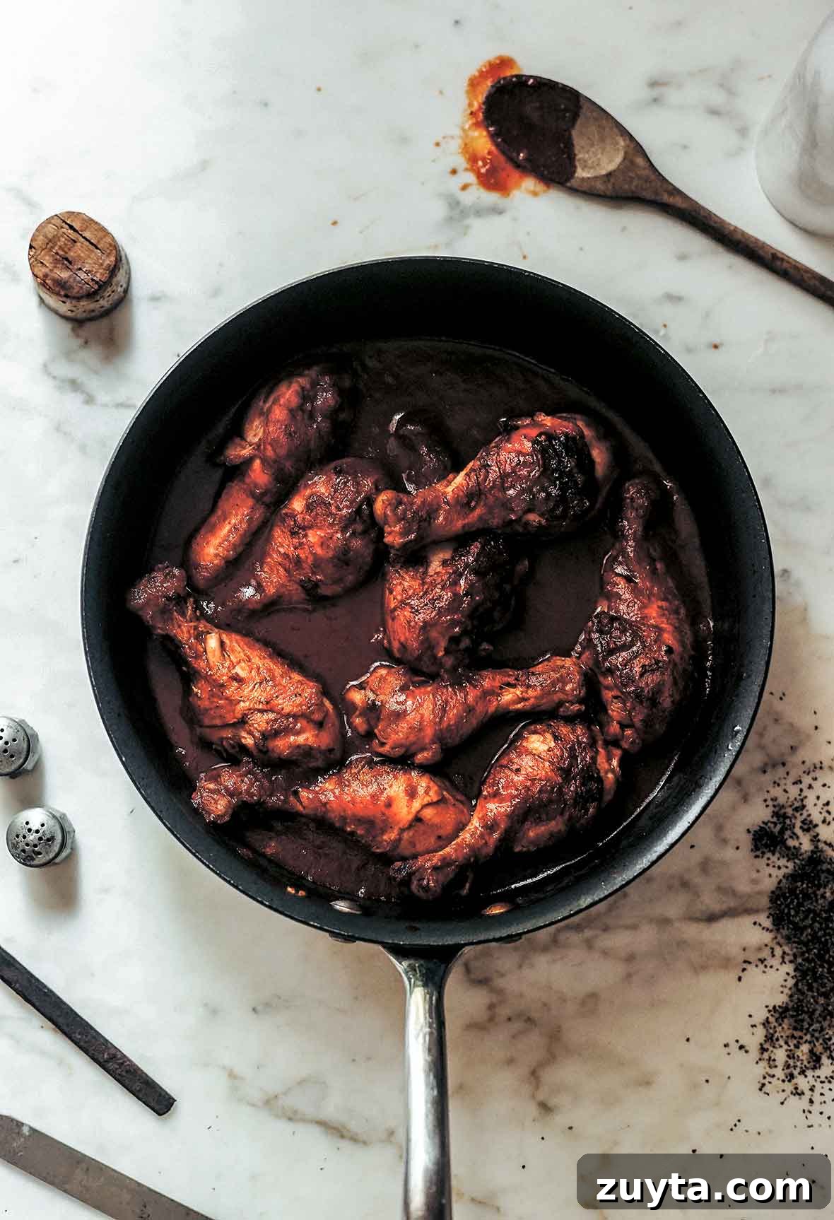 Braising Explained: What It Is and How to Braise 4 A skillet filled with chicken drumsticks braised in wine with a wooden spoon and wine cork lying beside the skillet.