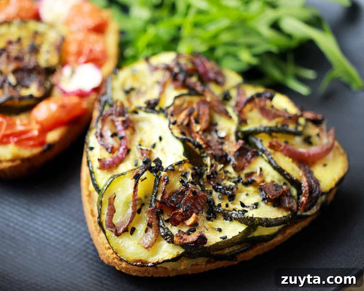photo of a heart-shaped vegan roasted vegetable tart on a black plate with rocket and a tomato tart behind.