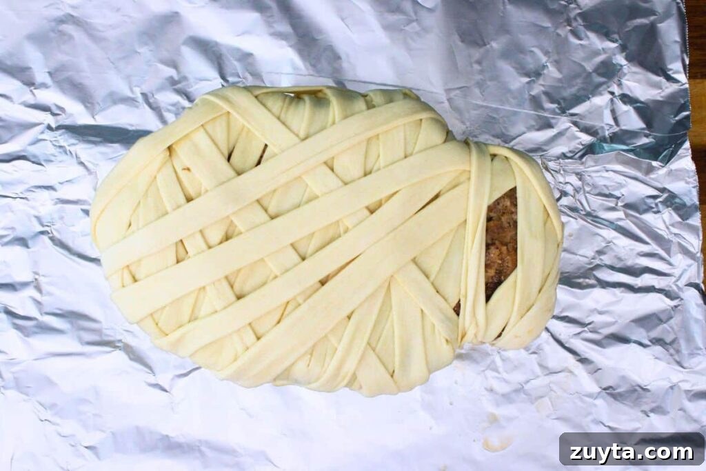 transfer partially cooked meatloaf on top of crescent dough and wrap strips as bandages around the mummy