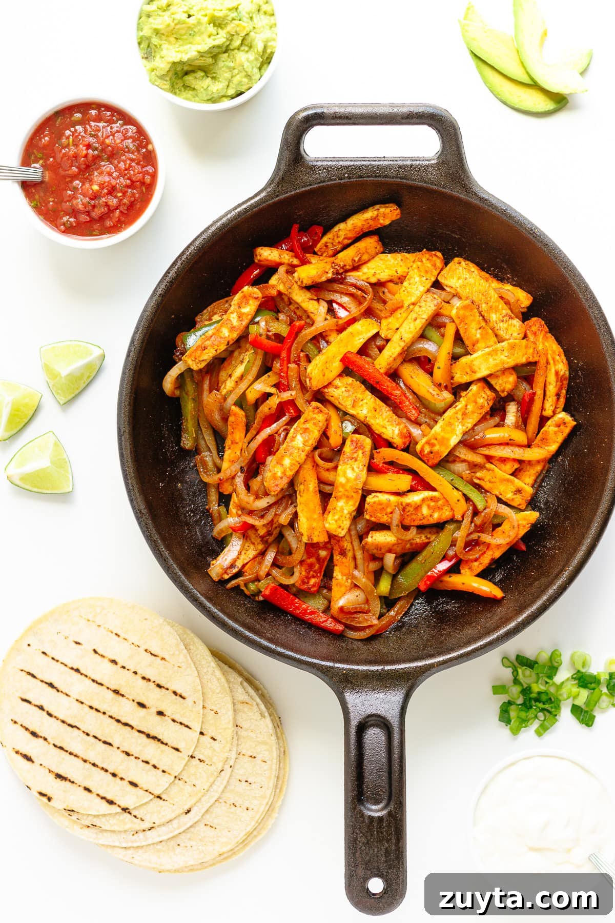 Grilled Halloumi Fajitas with Peppers and Lime 12 Halloumi veggie fajita mixture in a cast iron skillet with tortillas and a variety of toppings around it.