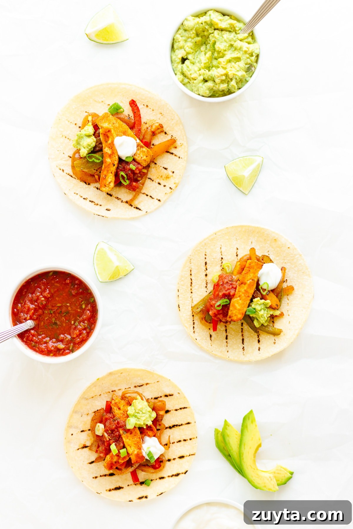Grilled Halloumi Fajitas with Peppers and Lime 3 Three halloumi fajitas on a white background with various toppings laid out around them.