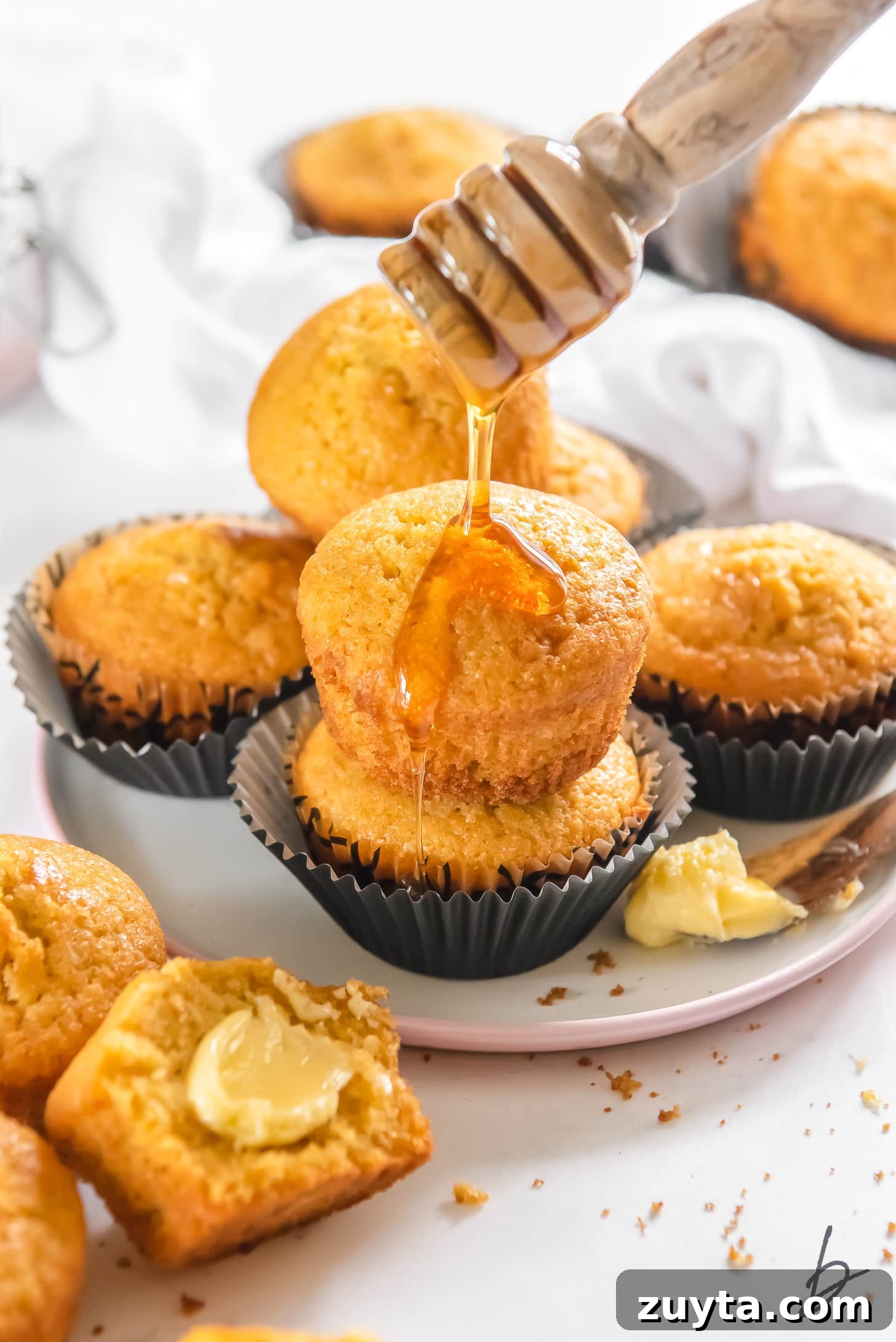 20-Minute Cornbread Muffins Recipe 4 honey being drizzled on top of two cornbread muffins stacked on plate with more muffins