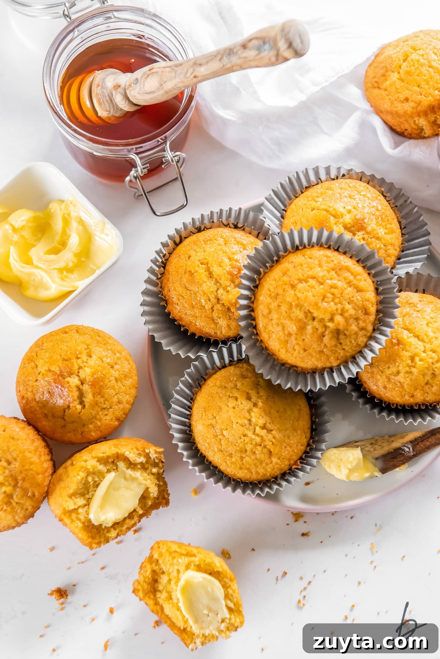 20-Minute Cornbread Muffins Recipe 5 honey jar next to plate of cornbread muffins and a cornbread muffin cut in half with butter