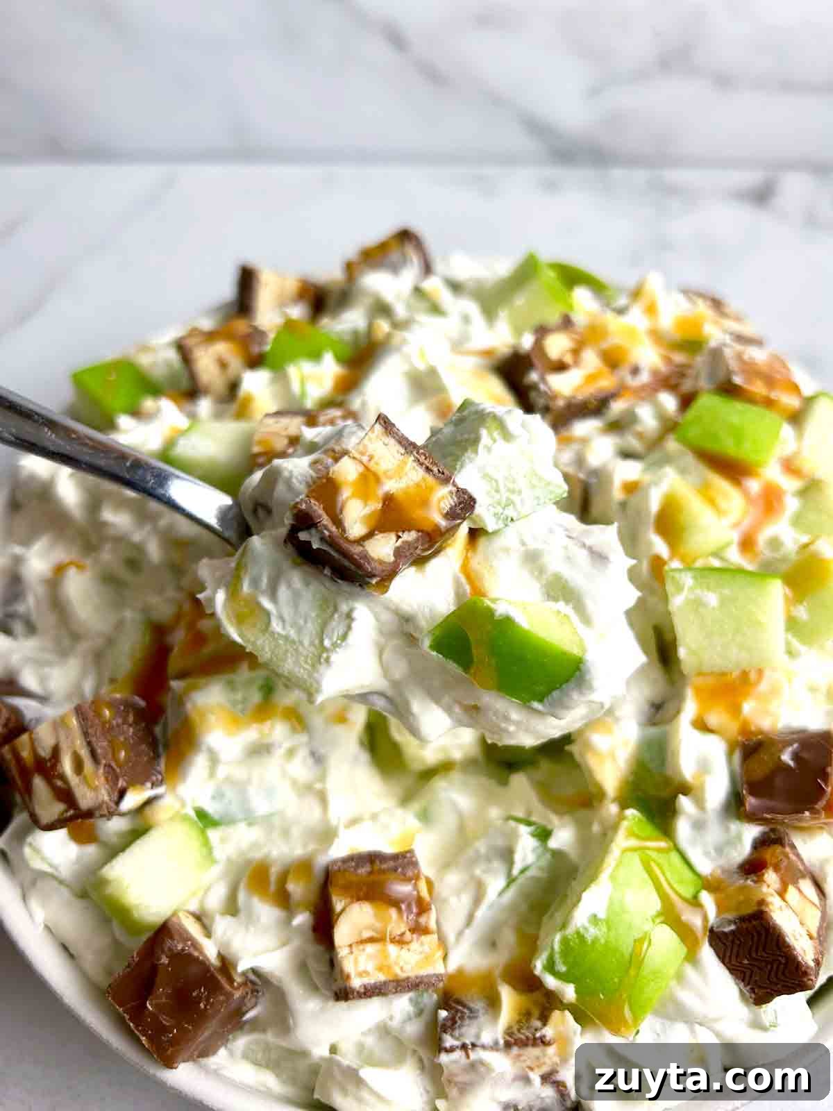 Snickers Salad Recipe: Creamy No-Bake Dessert with Apples 3 spoon lifting Snickers salad from bowl.