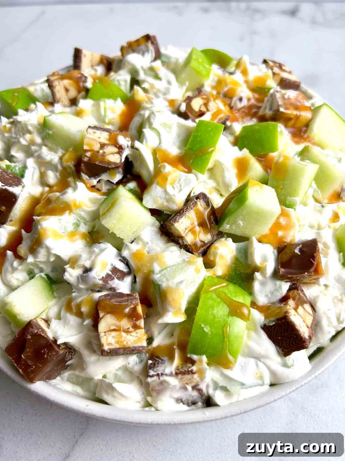 Snickers Salad Recipe: Creamy No-Bake Dessert with Apples 8 close up bowl of Snickers salad with caramel drizzled on top.