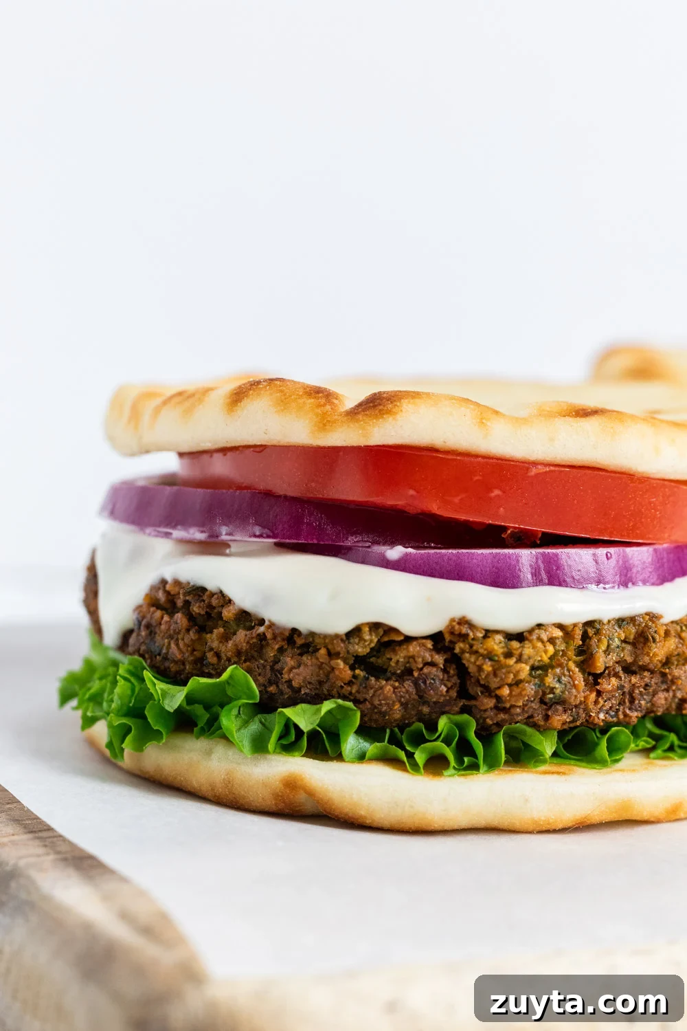 A close up view of a falafel burger with lettuce, tomato and onion.