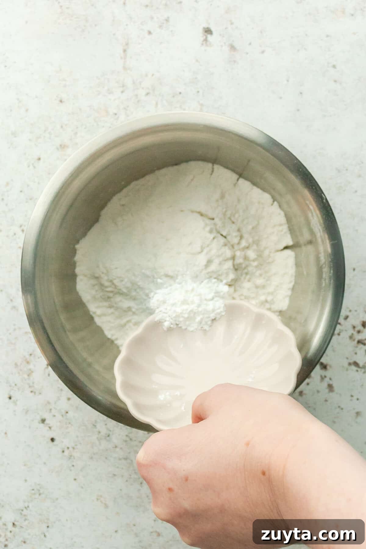 White Chocolate Peppermint Icebox Cookies Recipe 3 Baking soda is tossed over flour in a stainless steel bowl on a light gray surface.