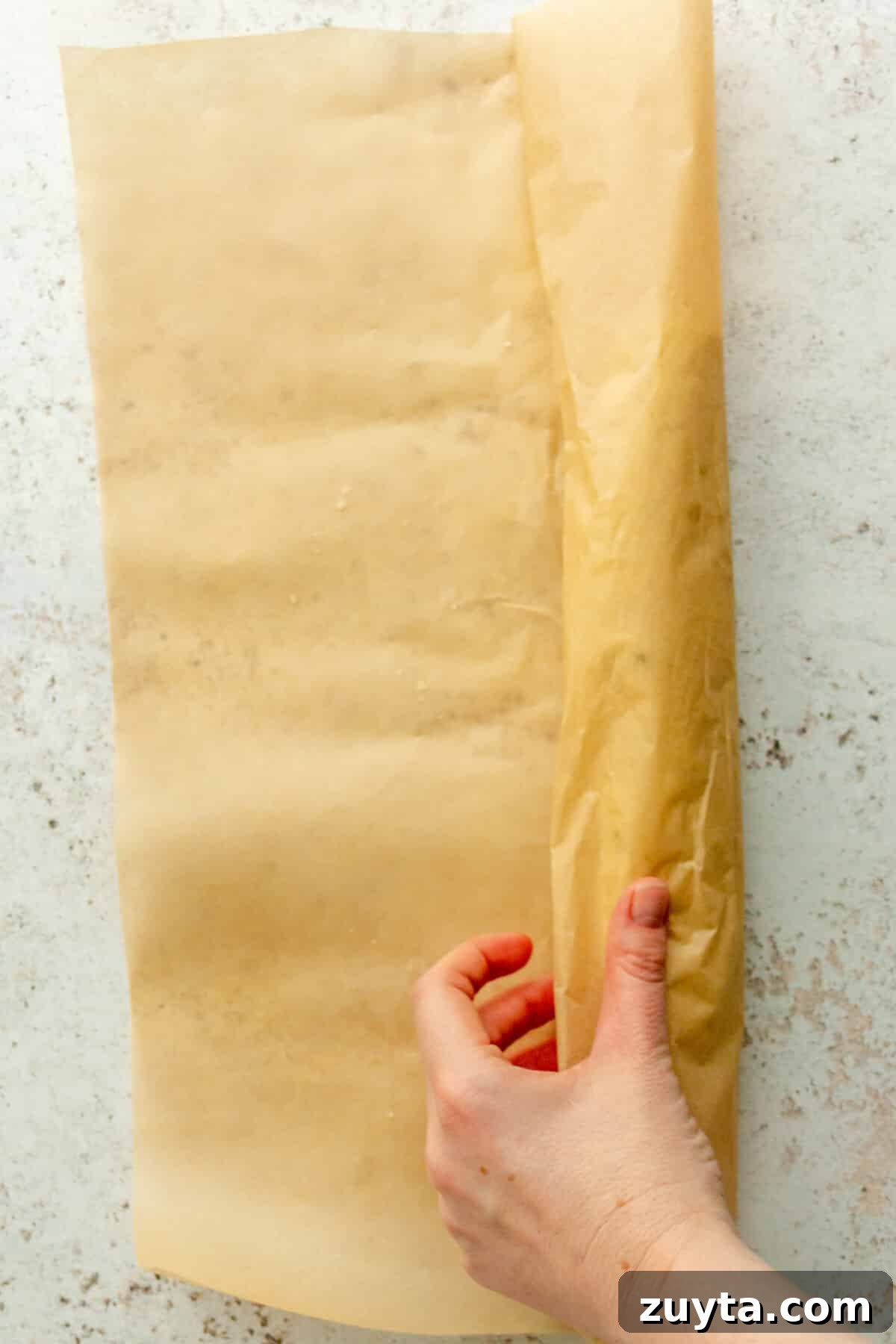 White Chocolate Peppermint Icebox Cookies Recipe 7 Cookie dough is rolled into a log in parchment paper on a light gray surface.