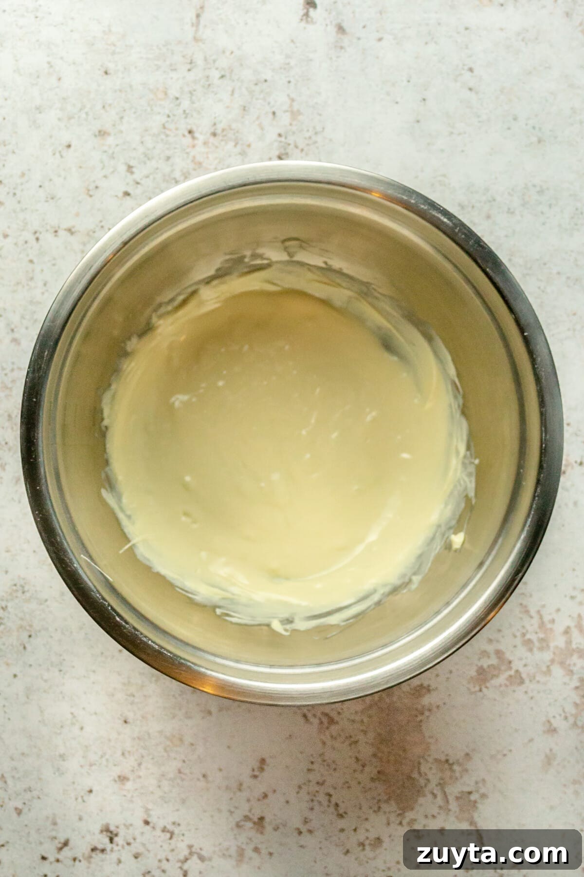 White Chocolate Peppermint Icebox Cookies Recipe 9 Melted chocolate sits in a stainless steel bowl on a light gray surface.