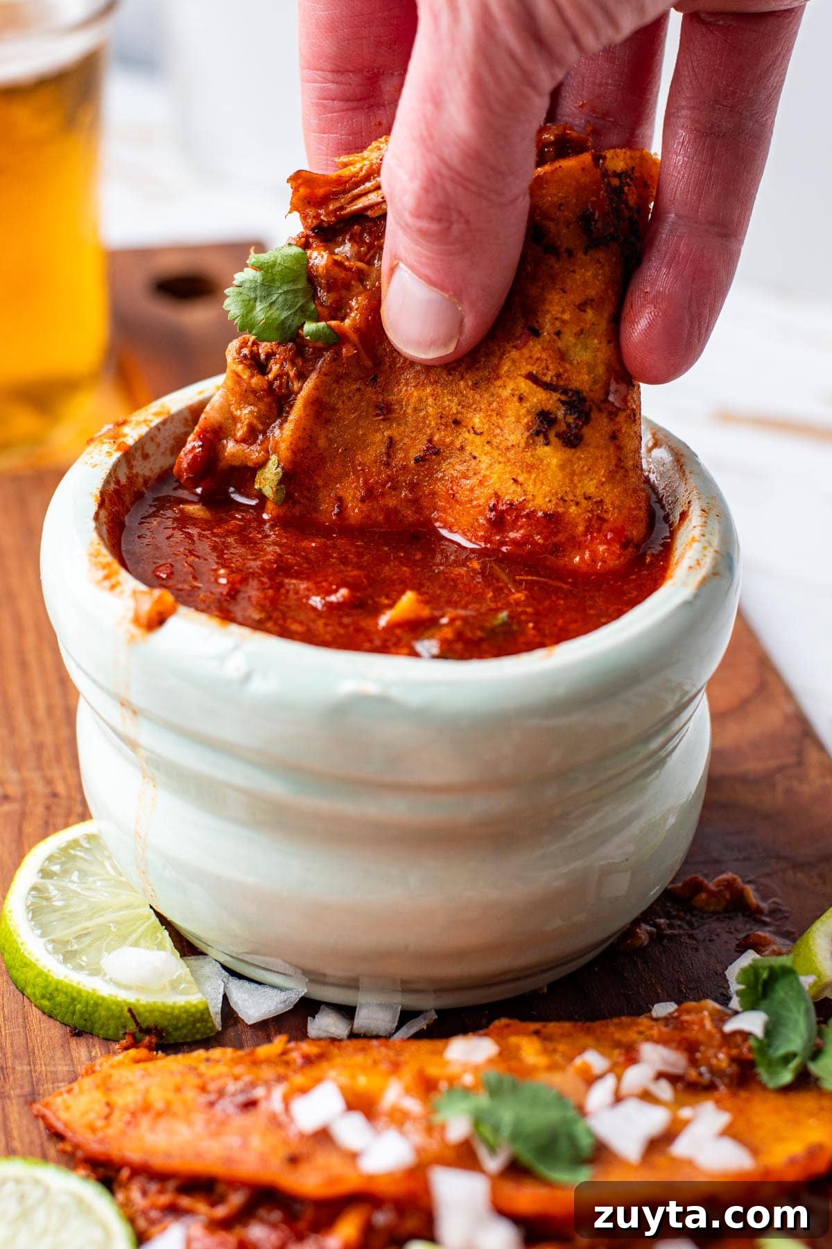 Chicken Birria Tacos Recipe with Consommé 3 A hand holding a chicken birria taco and dipping it in consomé sauce.