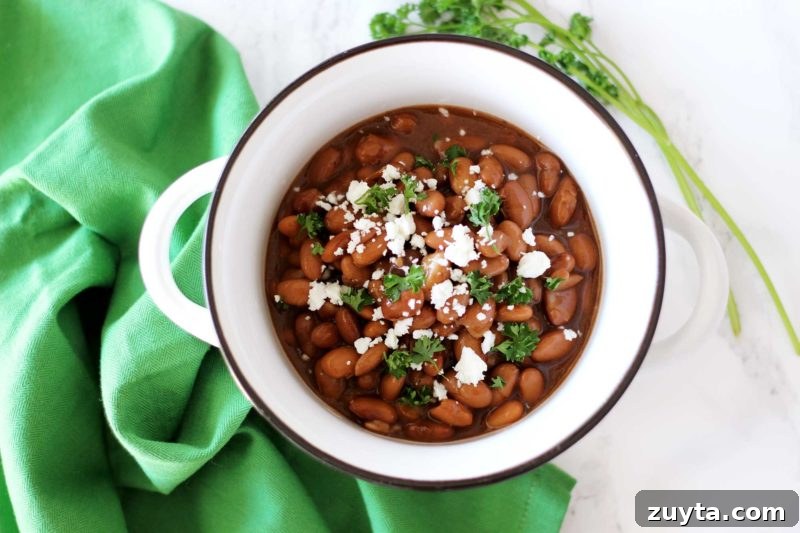 Slow Cooker Pinto Beans Recipe 10 Pinto Beans in a white bowl sitting on a white table with a green napkin topped with feta cheese and fresh parsley.