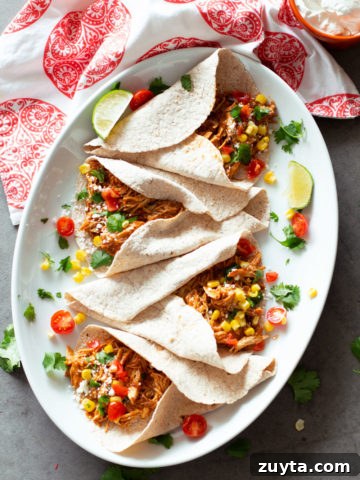 4 tacos filled with shredded salsa chicken, lime and salsa on plate.