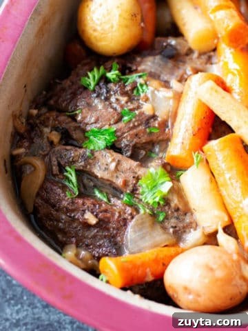 Cooked pot roast with carrots and potatoes in a red pyrex dish on counter top.