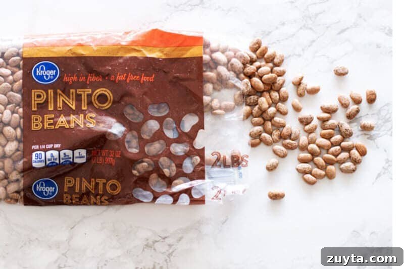 Slow Cooker Pinto Beans Recipe 6 A bag of dry pinto beans spread out on a white marble table top.