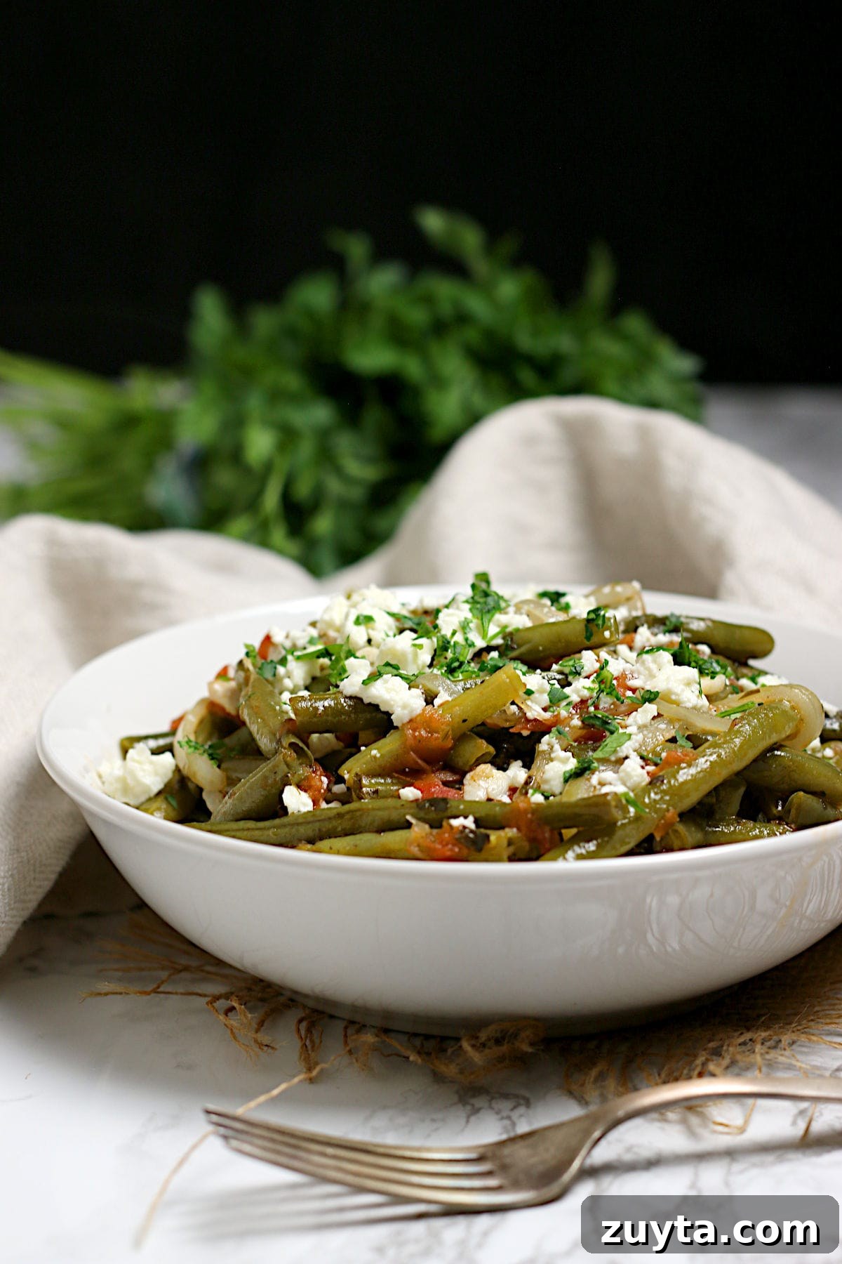 A closeup photo of Greek-Style Green Beans in a white bowl.