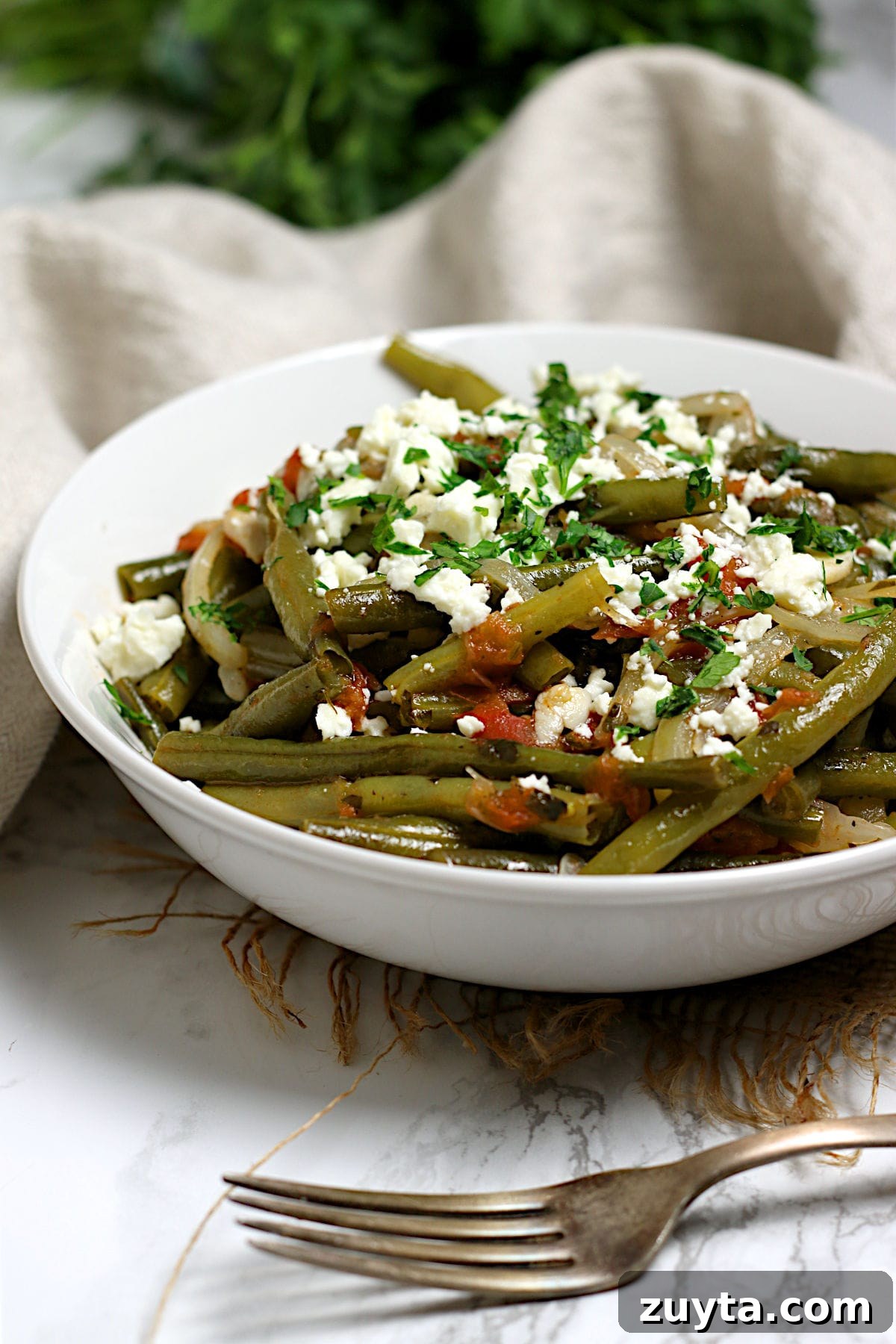 A closeup photo of Greek-Style Green Beans in a white bowl.