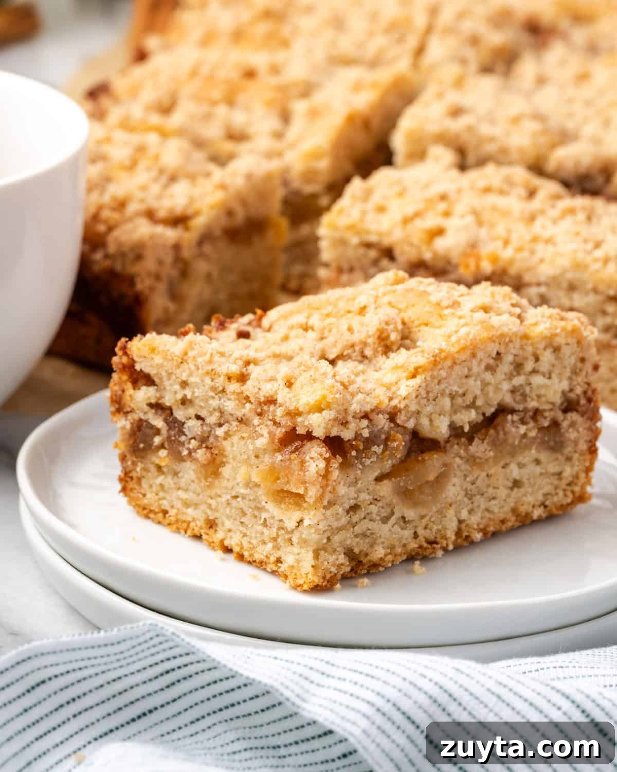 Moist Apple Cinnamon Coffee Cake Recipe 8 A single slice of apple cinnamon coffee cake on a small dessert plate next to a cup of coffee.