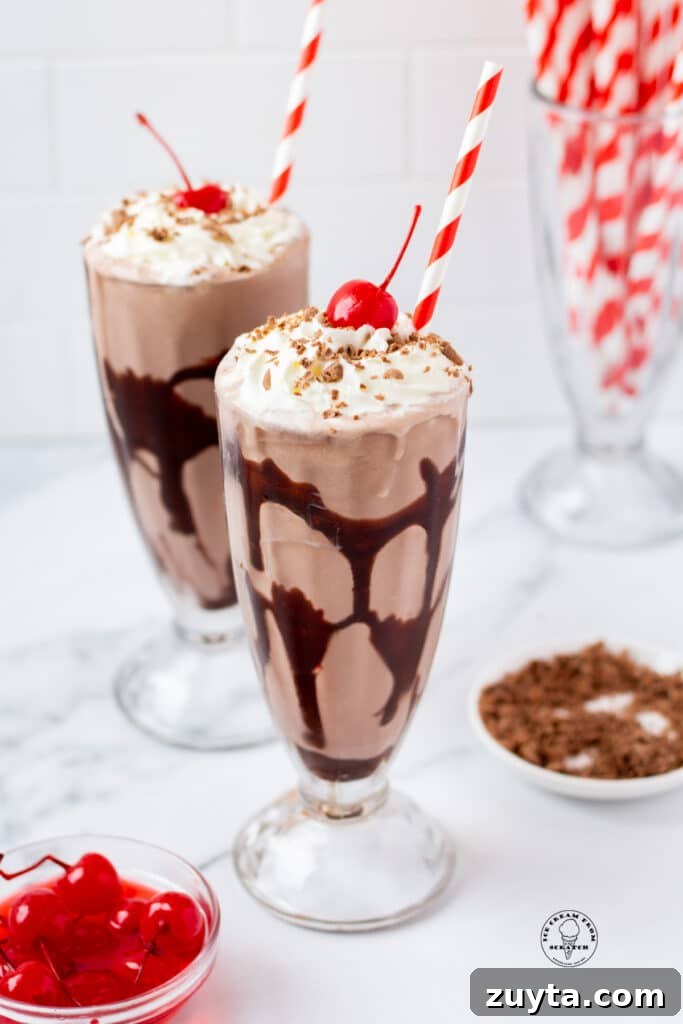 Homemade Milkshake Recipes for Every Craving 3 Two footed milkshake glasses filled with chocolate milkshake, swirled with chocolate syrup, and topped with whipped cream, cherries, and shaved chocolate
