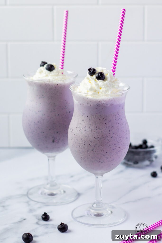 Homemade Milkshake Recipes for Every Craving 4 Two blueberry milkshakes in hurricane glasses with purple and white striped straws