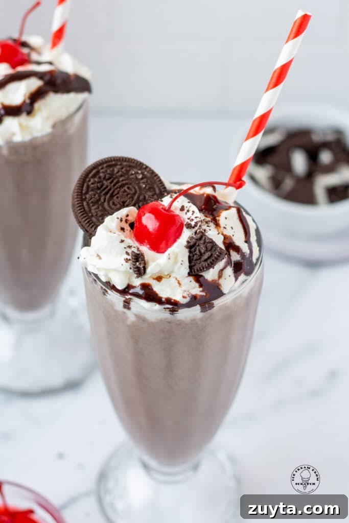 Homemade Milkshake Recipes for Every Craving 7 an oreo milkshake in a footed glass, topped with an oreo, oreo crumbs, whipped cream, and cherry.