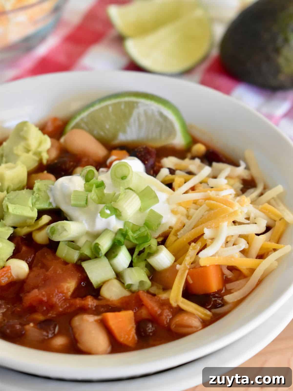 Slow Cooker Three-Bean Vegetarian Chili Recipe 3 White bowl filled with three bean vegetarian chili topped with sour cream, cheese, green onions, avocado and lime.