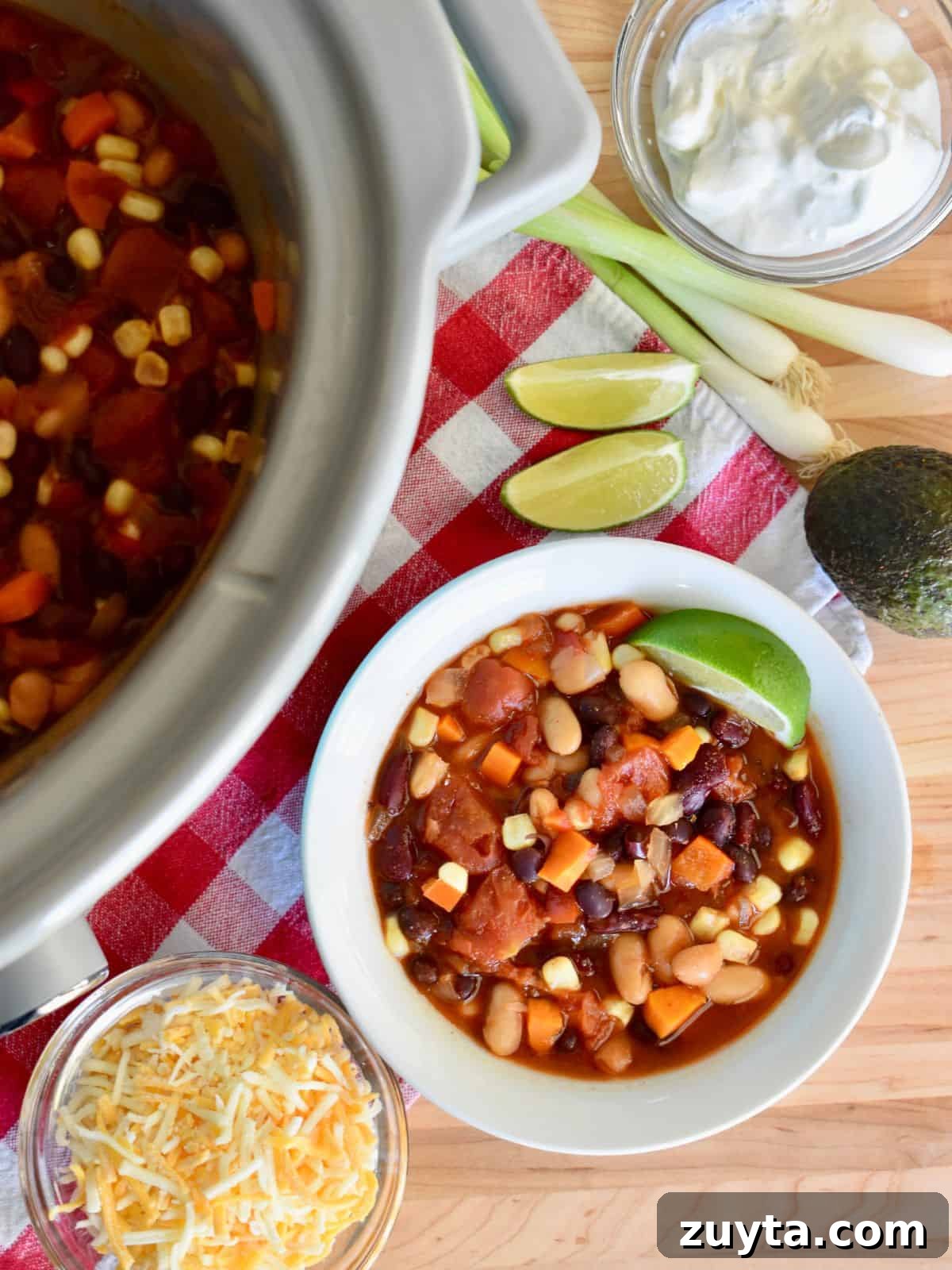 Slow Cooker Three-Bean Vegetarian Chili Recipe 7 Three Bean Vegetarian Chili in a bowl with a lime wedge and slow cooker filled with chili next to it.