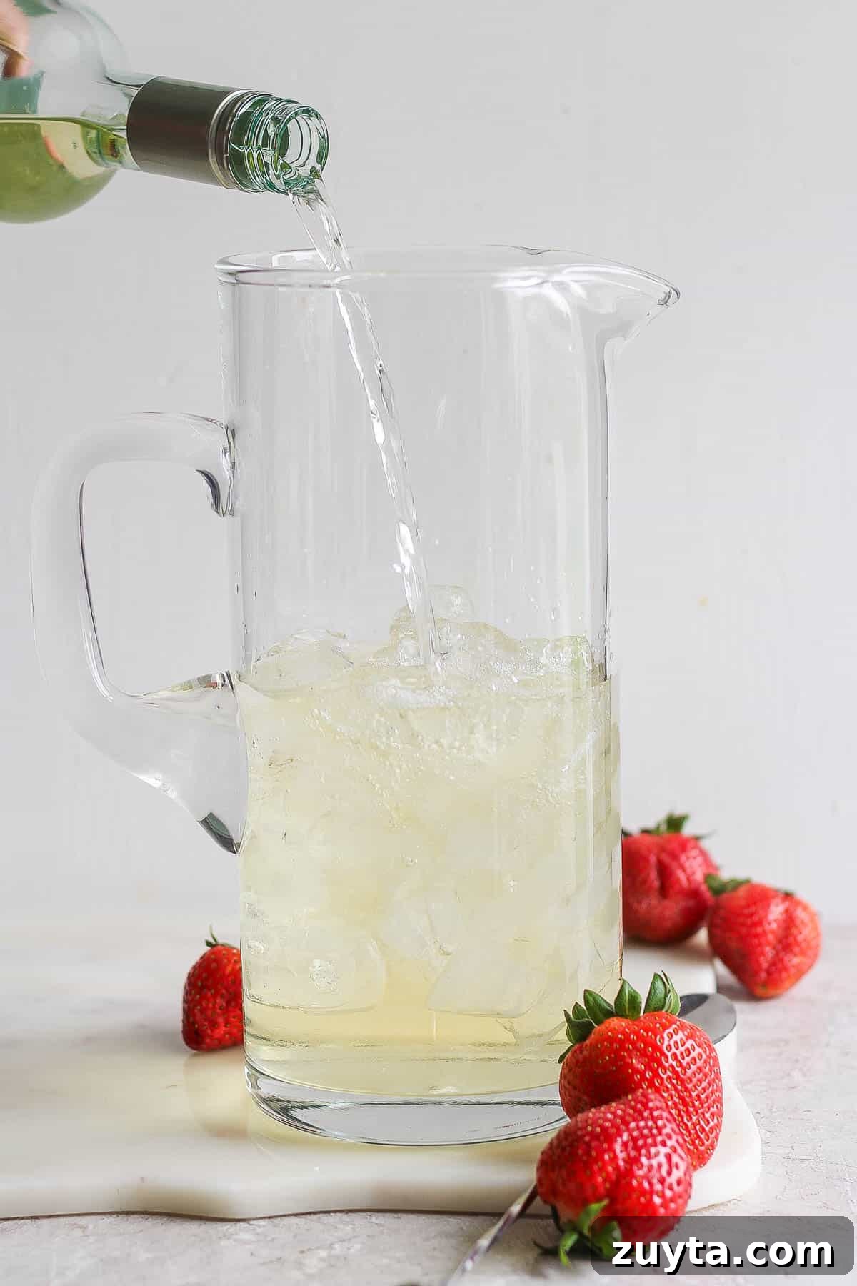 White Sangria Recipe with Citrus and Fresh Berries 4 A bottle of wine being poured into a glass pitcher.