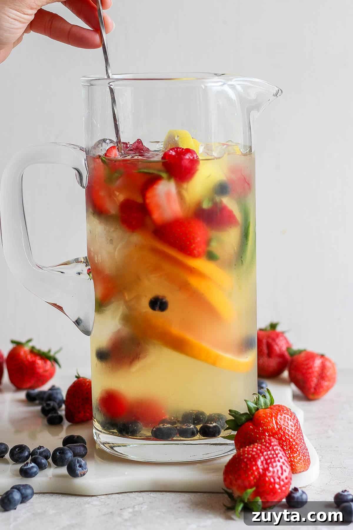 White Sangria Recipe with Citrus and Fresh Berries 6 A pitcher of sangria being stirred.