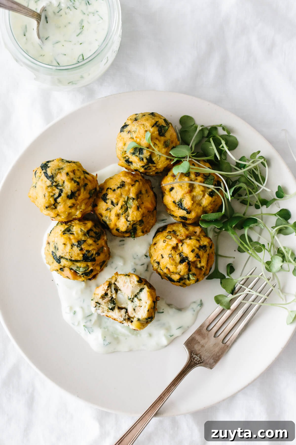 Over 60 Mediterranean Diet Recipes for Every Meal 64 Tuna meatballs on a plate with tzatziki sauce and micro greens.