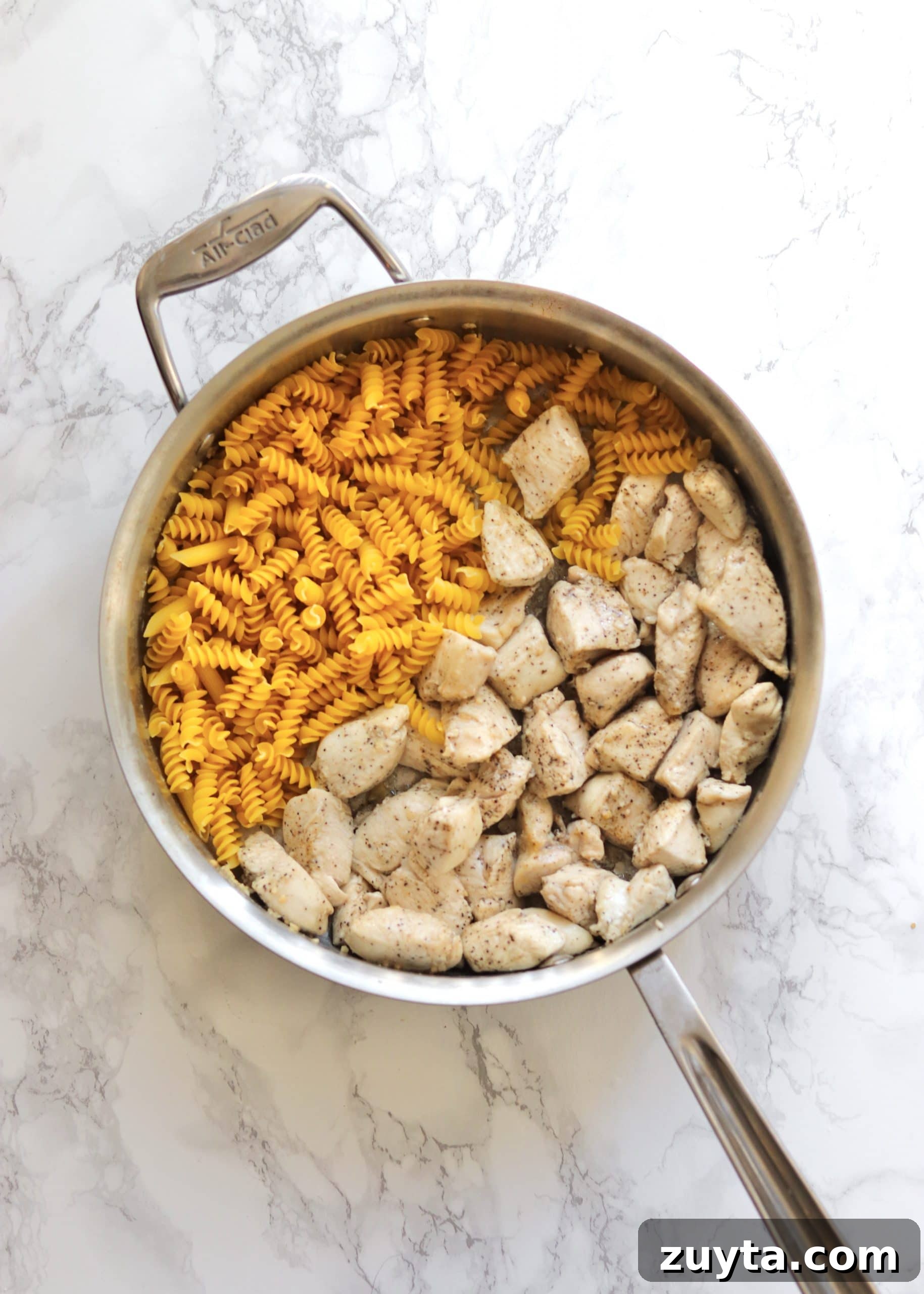 One-Pot Creamy Pesto Chicken Pasta Recipe 3 Cooked chicken breast chunks and uncooked pasta in a sauté pan