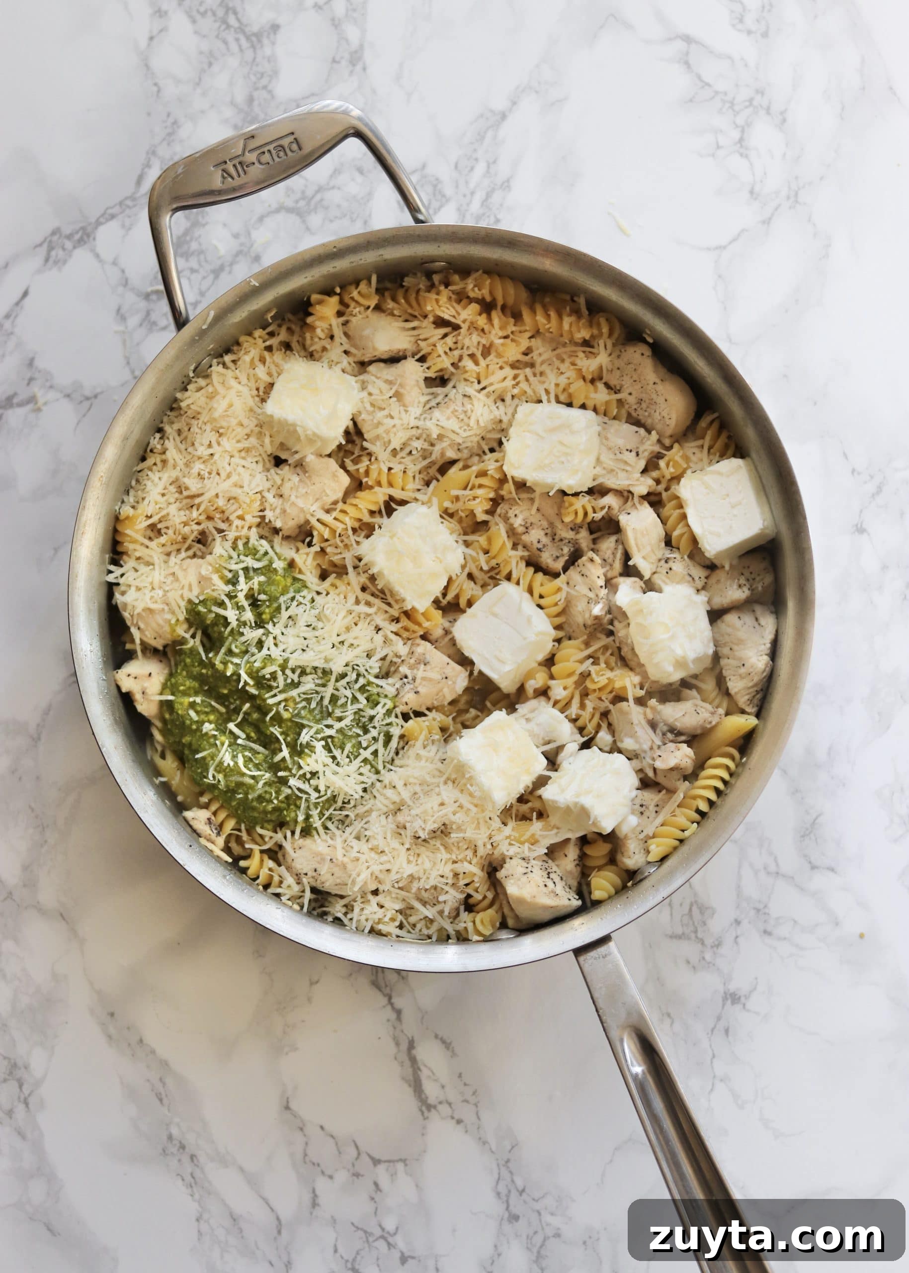One-Pot Creamy Pesto Chicken Pasta Recipe 4 Cooked chicken and pasta with cream cheese chunks, grated cheese, and pesto on top