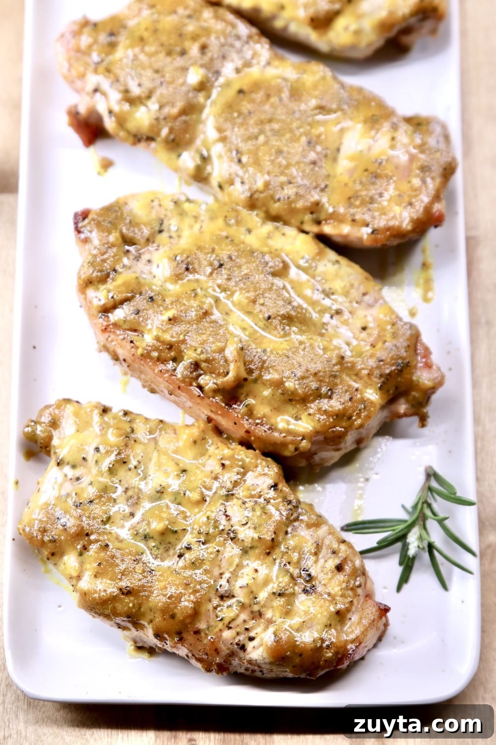 Rosemary Mustard BBQ Pork Chops are quick and easy to grill. The sweet and tangy mustard bbq sauce adds great flavor to the smoky pork. A must-try for dinner this week! Platter of mustard grilled pork chops with sprig of rosemary