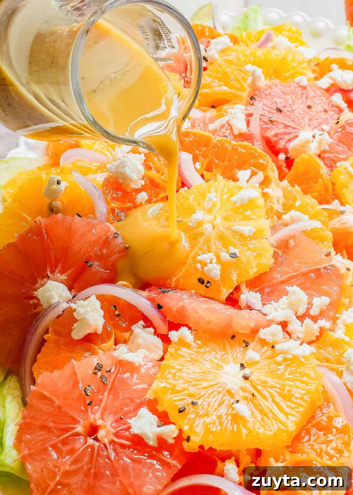 Zesty Citrus Salad with Orange, Grapefruit and Mint 4 A plate of oranges and grapefruits over salad with a dressing being poured on it.