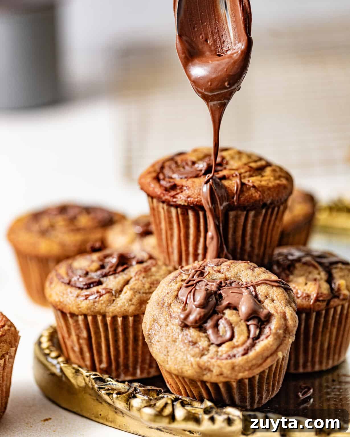nutella on a spoon being drizzled on top of banana muffins.