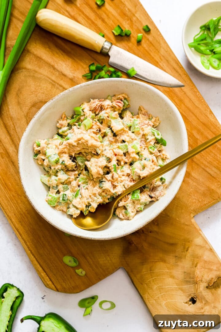 Spicy tuna salad in a white bowl, mixed with a gold spoon